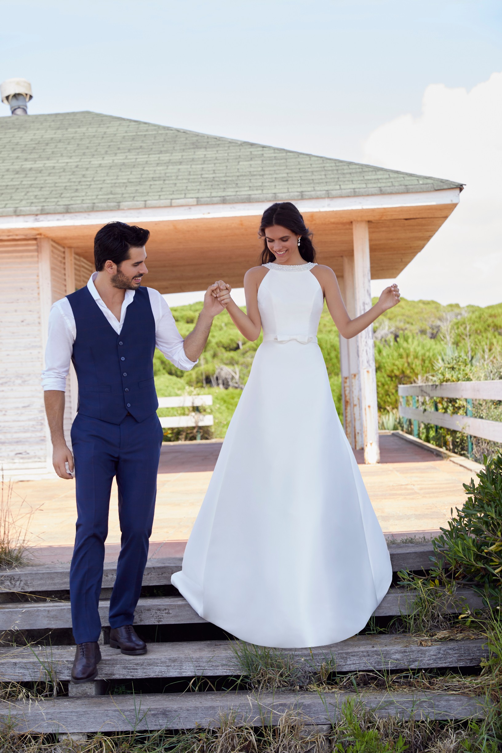 Man and Woman walking down steps outside villa while woman wears classic mikado ballgown wedding dress with high neckline and embellished belt