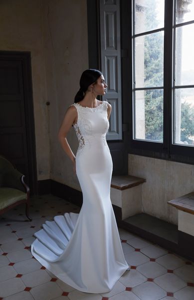 Model stood by a stately home window wearing Ronald Joyce 18451, a sleeveless fit and flare wedding dress with a high neckline and delicately beaded shoulder appliques