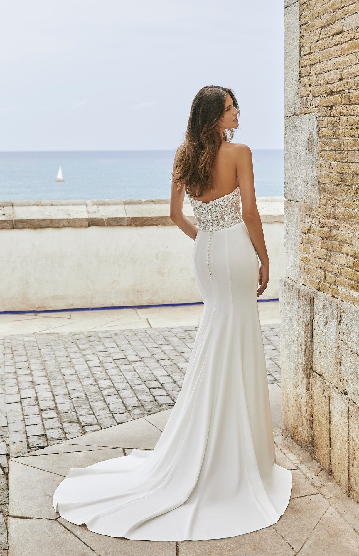 Back profile of model in Ronald Joyce destination wedding dress style 18604, a strapless dress with a beaded sweetheart bodice and plain fit and flare skirt.