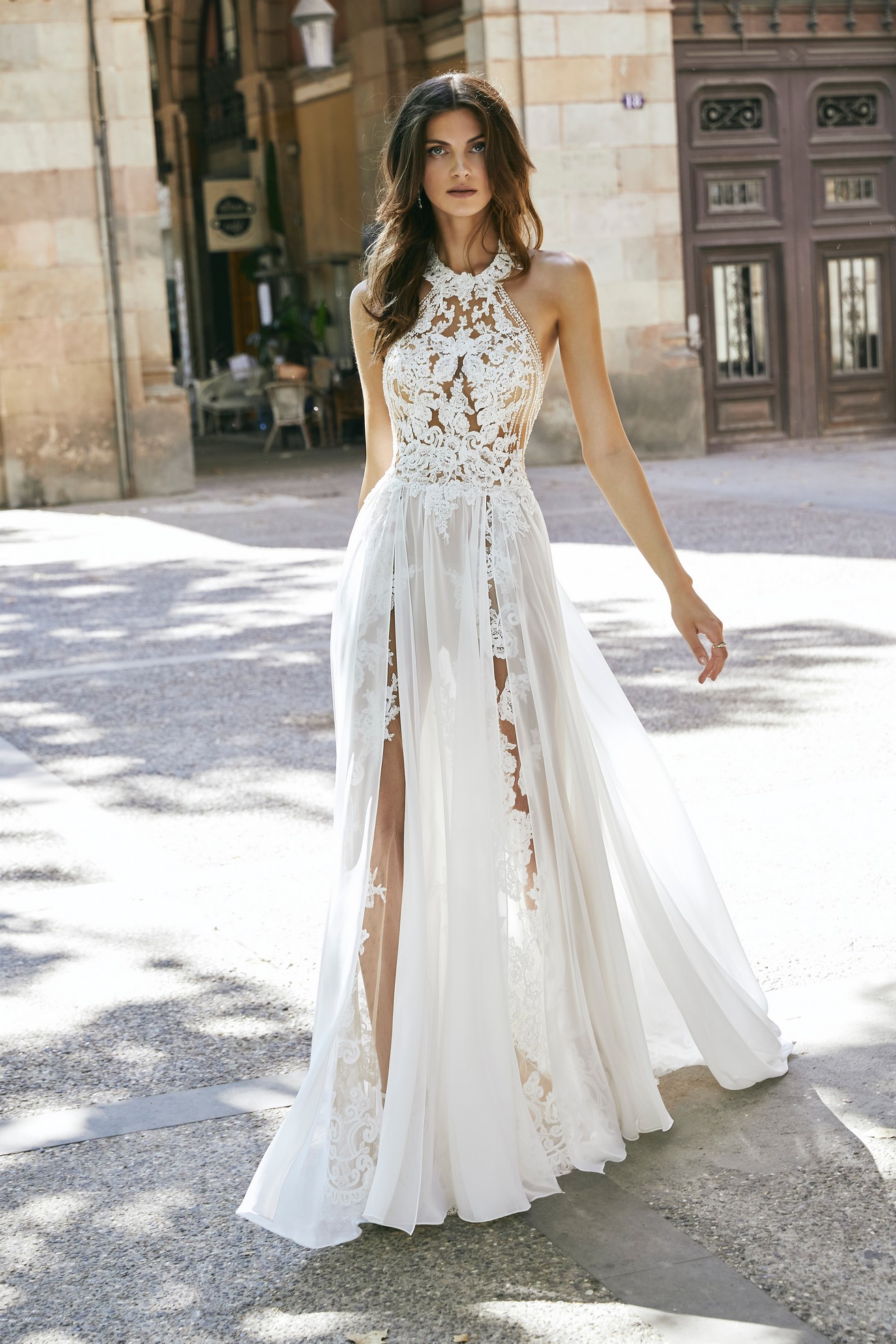 Front profile of model in Ronald Joyce destination wedding dress style 18611, a lace illusion halter neck dress with plain chiffon skirt and 2 splits. 