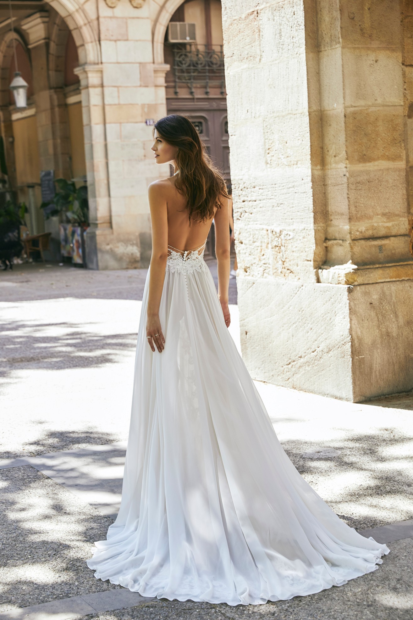 Back profile of model wearing the Ronald Joyce Victoria Jane wedding dress style 18611, a boho lace illusion halter neck wedding dress with contrasting chiffon skirt and splits. 