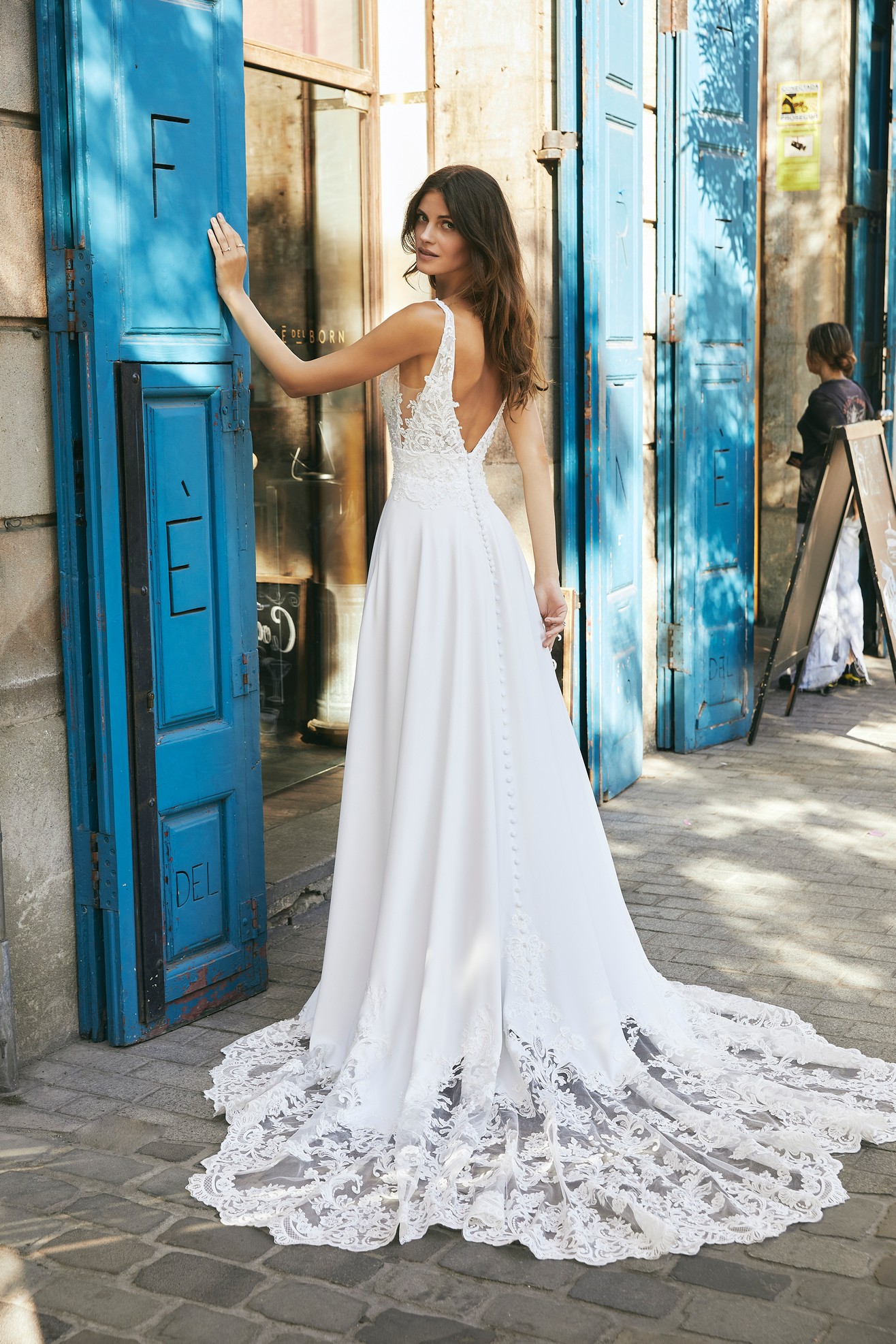 Back profile of model in Ronald Joyce destination wedding dress style 18618, a crepe and lace A-line wedding dress with a plunging v-neckline and open back