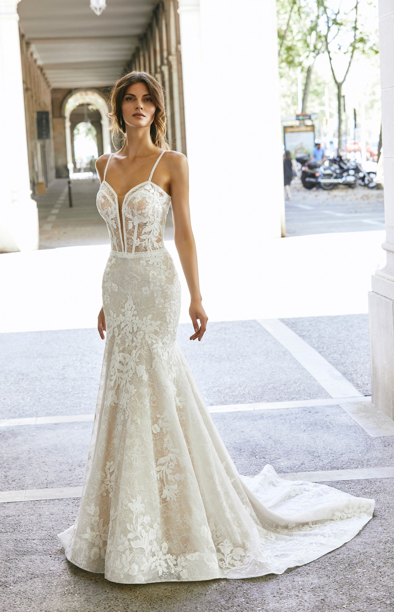 Model stood outside in Ronald Joyce Victoria Jane style 18620, a striking lace and tulle fit and flare wedding dress with a plunging sweetheart neckline and delicate straps