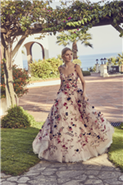 Woman standing in front of sea landscape wearing blush pink wedding dress decorated with colourful 3D floral detail