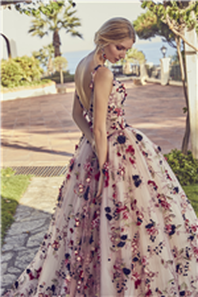 Blonde lady standing in front of scenic landscape garden wearing pink ballgown wedding dress with brightly coloured flower details