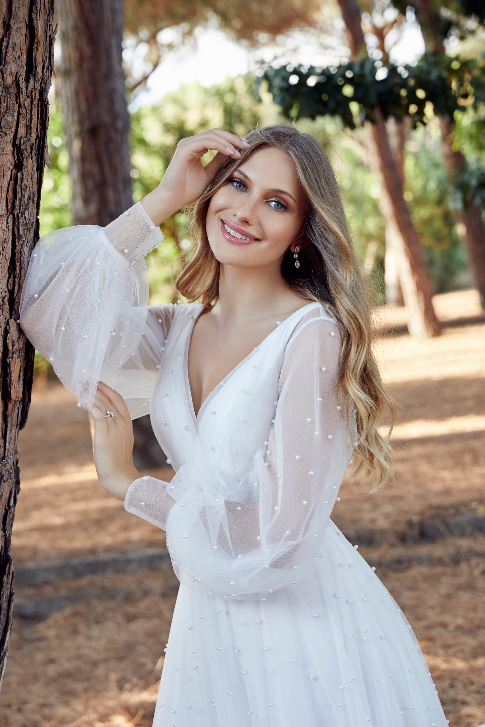 Close up thumbnail of model sat outside in Ronald Joyce style 69531, beaded bodice wedding dress with delicate straps and a ruffled organza ballgown skirt