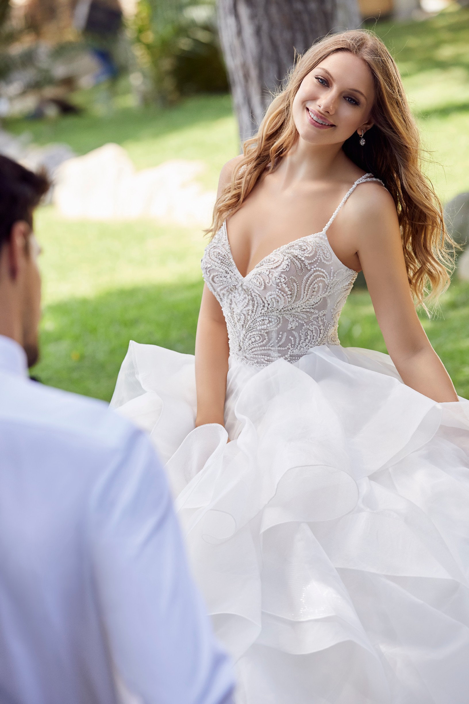 Close up of model sat outside in Ronald Joyce style 69531, beaded bodice wedding dress with delicate straps and a ruffled organza ballgown skirt