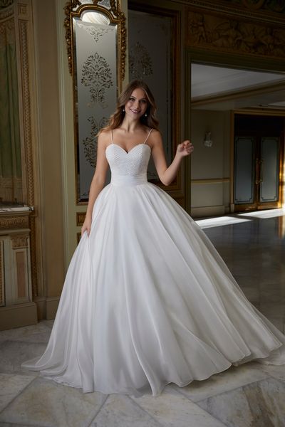 Blonde woman standing in extravagant ballroom wearing princess ballgown wedding dress with pearl bodice details