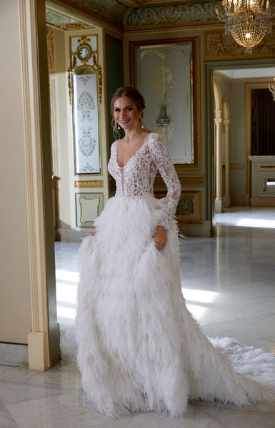 Woman standing in decorated villa wearing beaded bodice with long sleeves and full feather skirt