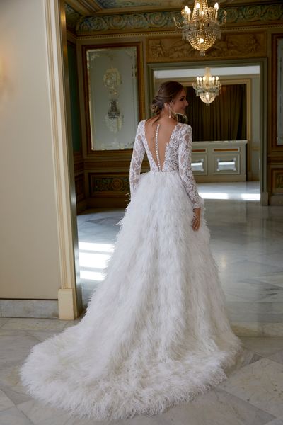 Woman standing in ballroom wearing backless wedding dress with ballgown feather skirt