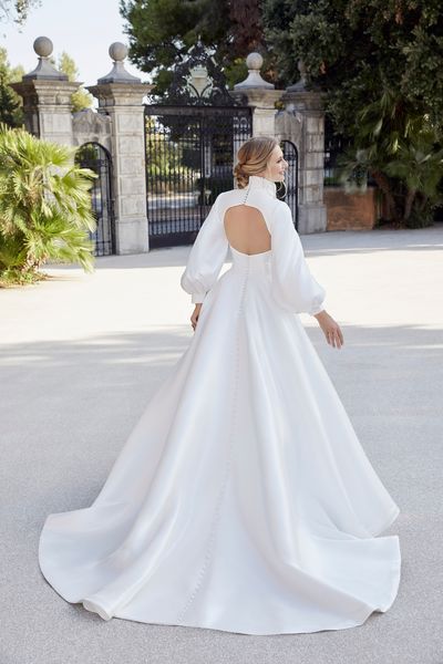 Back image of blonde lady standing in front of ornate gates and garden wearing ballgown wedding dress with keyhole back detail