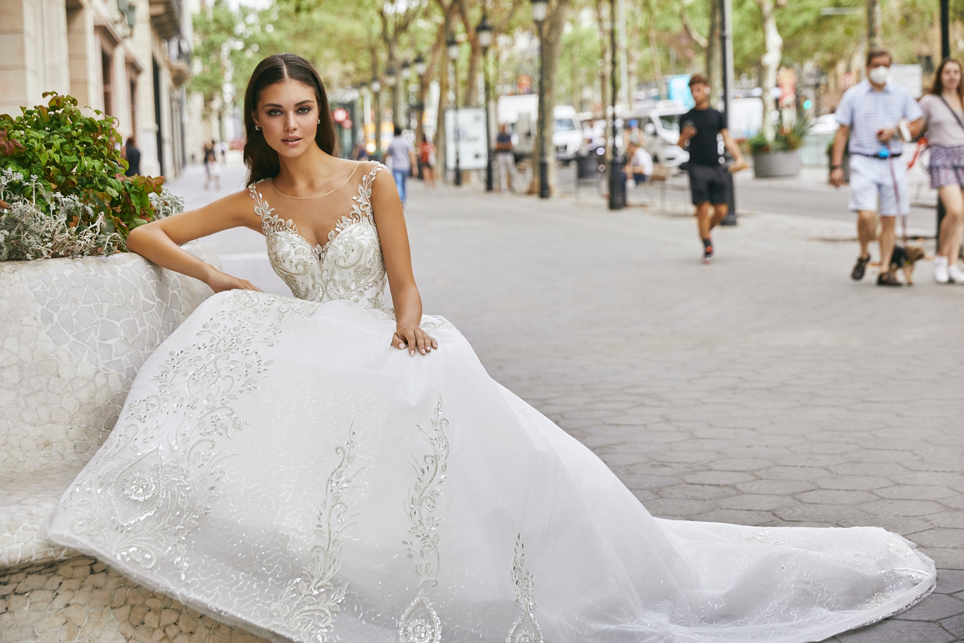 Model sat in a busy Italian street wearing Ronald Joyce style 69720, a beautiful ballgown wedding dress with a sweetheart neckline and illusion straps